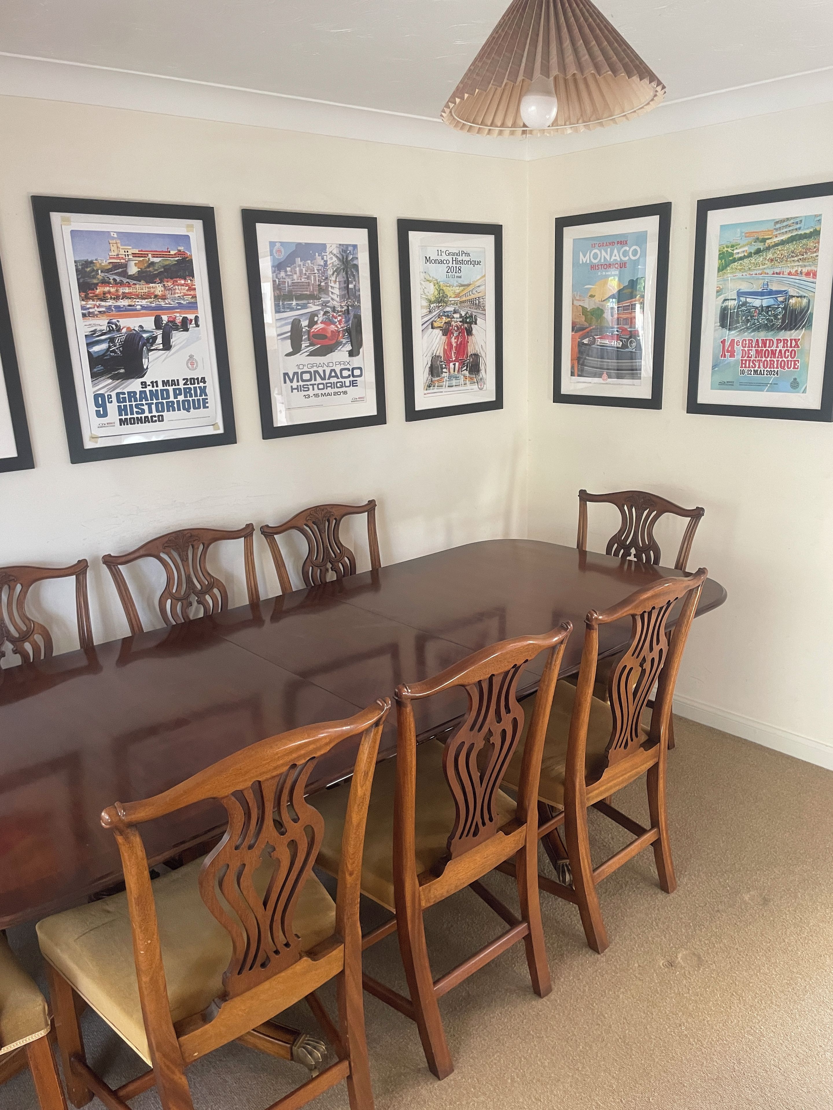 A conference room with a long wooden table and six chairs, framed posters on the wall, and a ceiling light fixture.