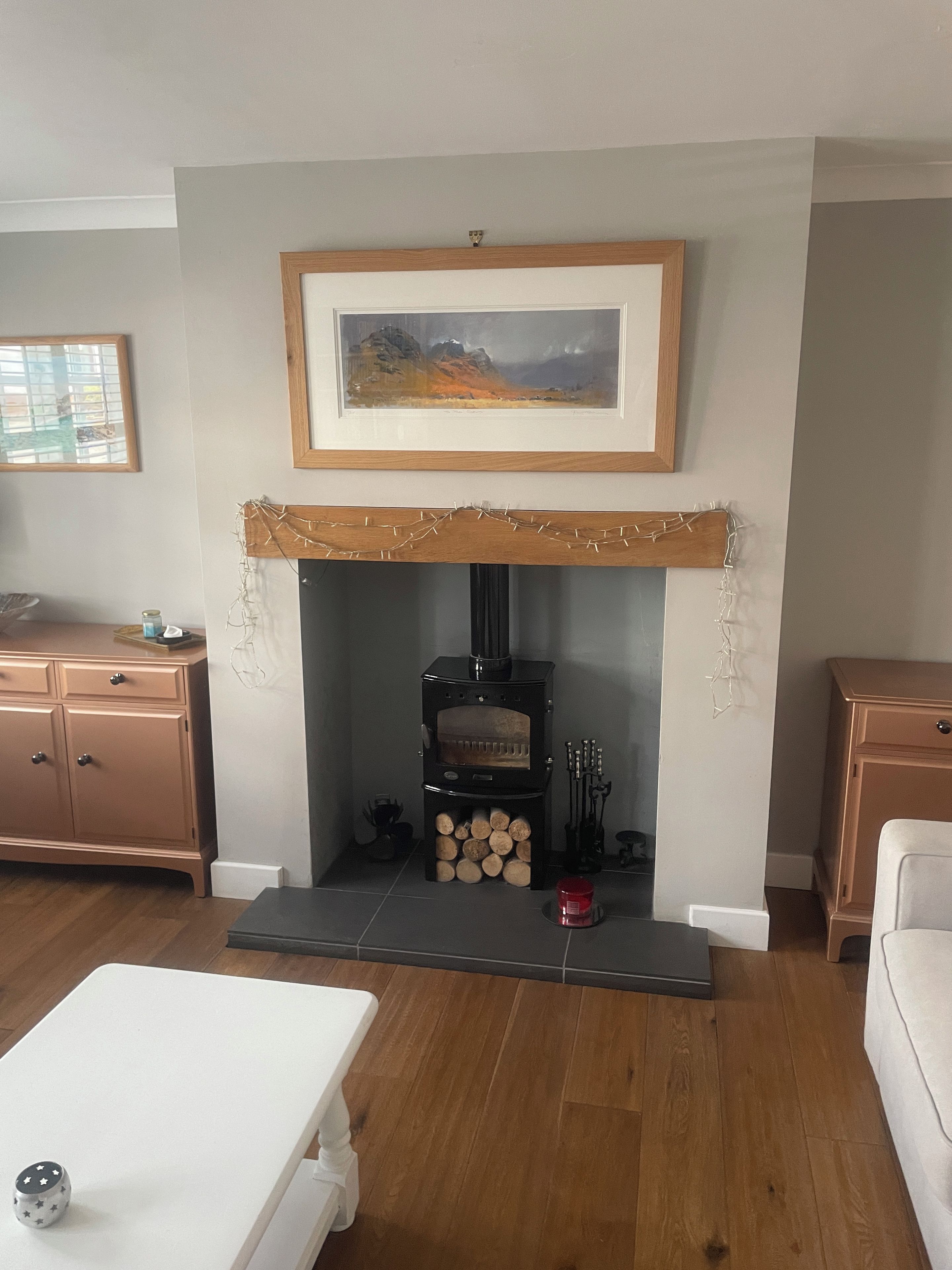 A living room with a fireplace, a painting above it, and a wooden cabinet to the left.