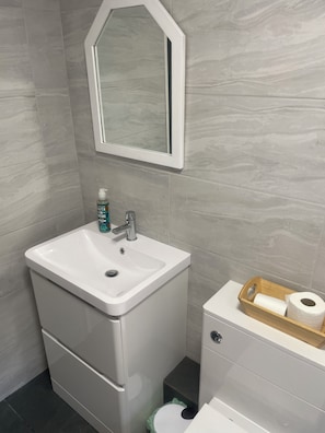 A bathroom with a white sink, a mirror, a toilet, and a wooden tissue holder. - Quiet 4 bedroom home with fast WiFi and parking.
Decorated to a high standard (Newton Flotman)