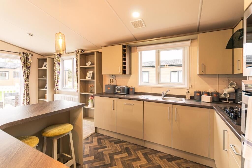 Une cuisine moderne avec un parquet disposé en chevrons, un four à micro-ondes encastré et une fenêtre donnant sur l’extérieur.