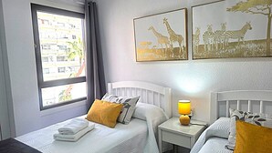 A hotel room with two beds, a window with a view of buildings, and two wall-mounted animal-themed artworks. - Librada Home Playa Las Americas (Playa de las Américas)