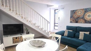 A living room with a staircase, a flat-screen TV, a round white table, and a blue sofa. - Librada Home Playa Las Americas (Playa de las Américas)