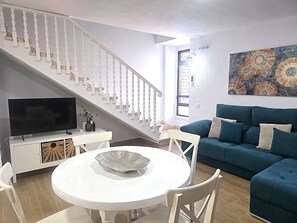 A living room with a staircase, a flat-screen TV, a round white table, and a blue sofa. - Librada Home Playa Las Americas (Playa de las Américas)