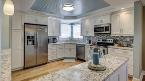 Une cuisine moderne avec des armoires blanches, des appareils en acier inoxydable, un comptoir en marbre et un design de plafond original.