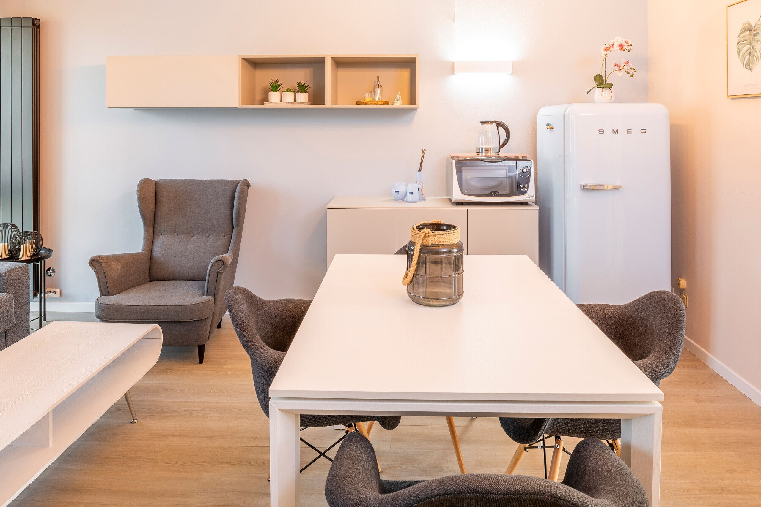 A modern kitchen with a white table, grey chairs, a microwave, and a fridge.