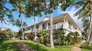A two-story building with a balcony, surrounded by palm trees and tropical plants. - Ocean View 6BR, 2 Condos for 16 in Koloa! (Koloa)