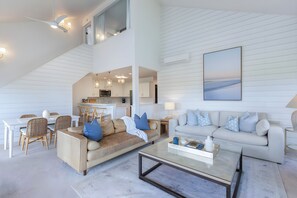 Een ruime woonkamer met een hoge plafond, een eethoek, een bank en een salontafel.