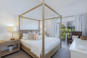 Een hemelbed met houten frame, een nachtkastje met lamp en een stoel met kussen.
