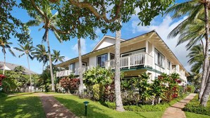 A two-story building with a balcony, surrounded by palm trees and tropical plants. - Poipu Kai - 6BR Ocean View, 2 Condos - Sleeps 16 (Koloa)