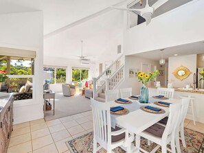 A spacious living area with a dining table, white furniture, and a staircase leading to an upper level. - Poipu Kai - 6BR Villas, Pool - Sleeps 16 (Koloa)