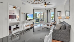 Una habitación de hotel moderna con balcón, zona de comedor, sofá y televisión.