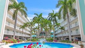Un hotel con piscina central rodeado de palmeras y un edificio de varios pisos con balcones.
