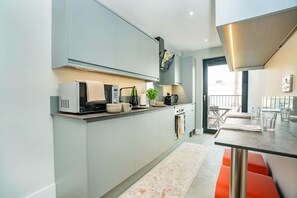 Una cocina moderna con armarios de colores claros, microondas integrado y una zona de comedor con mesa y sillas.