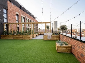A rooftop garden with artificial grass, wooden planters, and a wooden pergola.