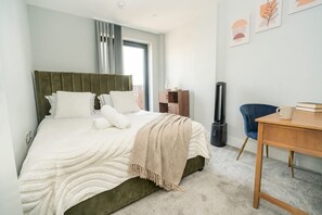 Una habitación de hotel con cama, escritorio, silla, radiador y una obra de arte en la pared.