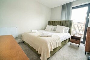 A hotel room with a bed, a wooden nightstand, a window with curtains, and a view of the outside.