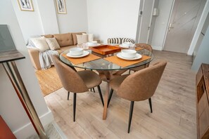 Un área de comedor con una mesa de vidrio, cuatro sillas y un sofá al fondo.
