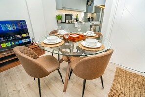 Un comedor moderno con una mesa de vidrio, cuatro sillas y un televisor que muestra un evento en vivo.