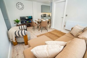 Una sala de estar moderna con un sofá, un televisor, un comedor y una cocina al fondo.
