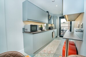 A modern kitchen with a microwave, kettle, and a small dining area with a table and chairs.