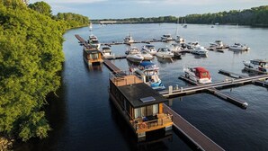 Un port de plaisance avec des bateaux amarrés, une structure flottante dotée d’une terrasse et une rive bordée d’arbres.