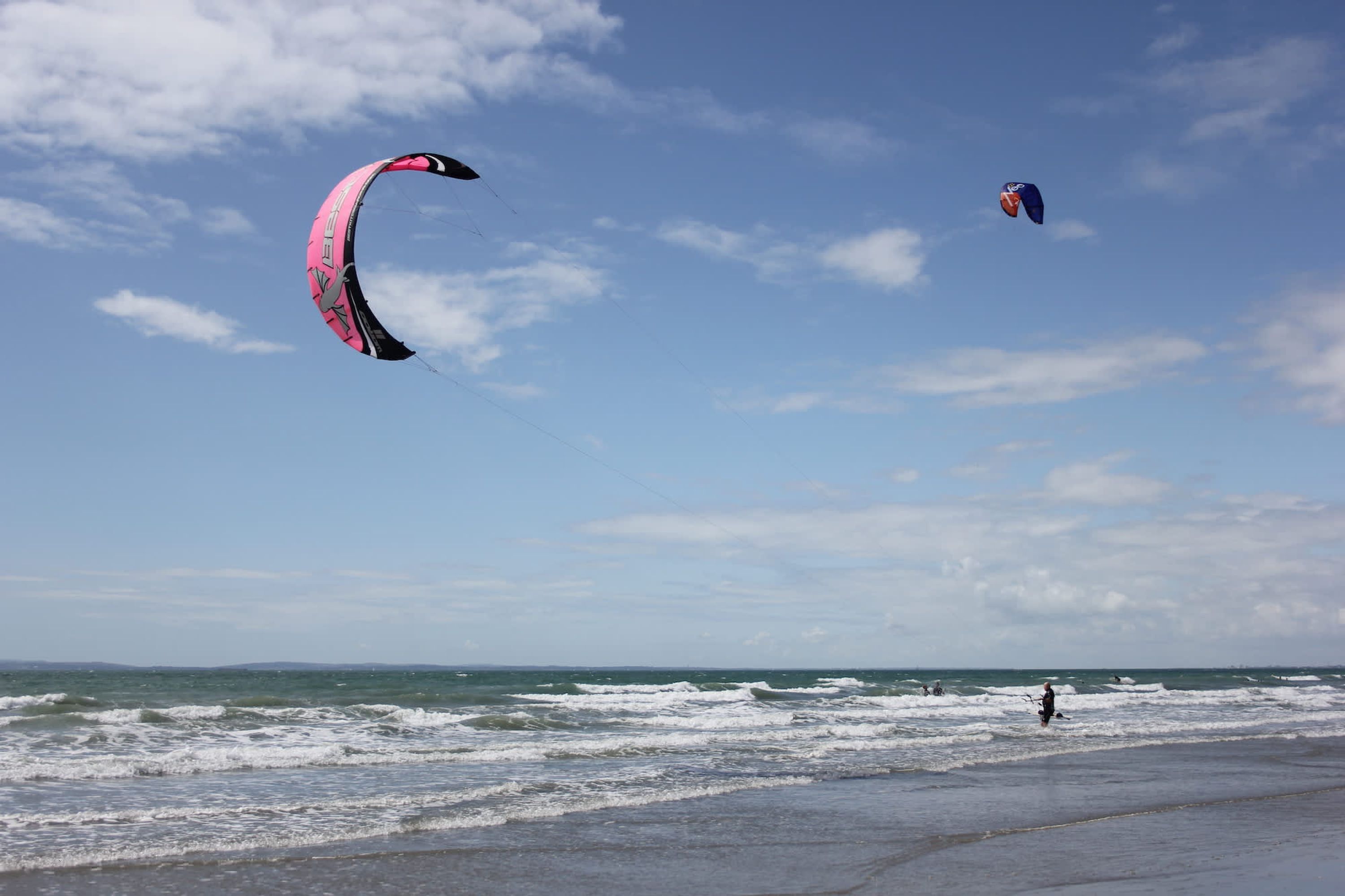 A beach with waves, a person, and a kite.