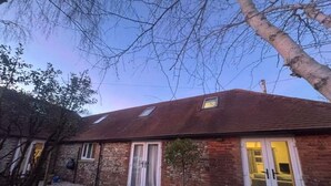 A brick building with a sloped roof, a small window, and a door with glass panels. - Buttercup - Super King Ensuite Room in Sidlesham (Chichester)