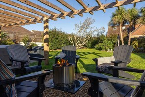 En udendørs terrasse med Adirondack-stole, pejse og pergola.