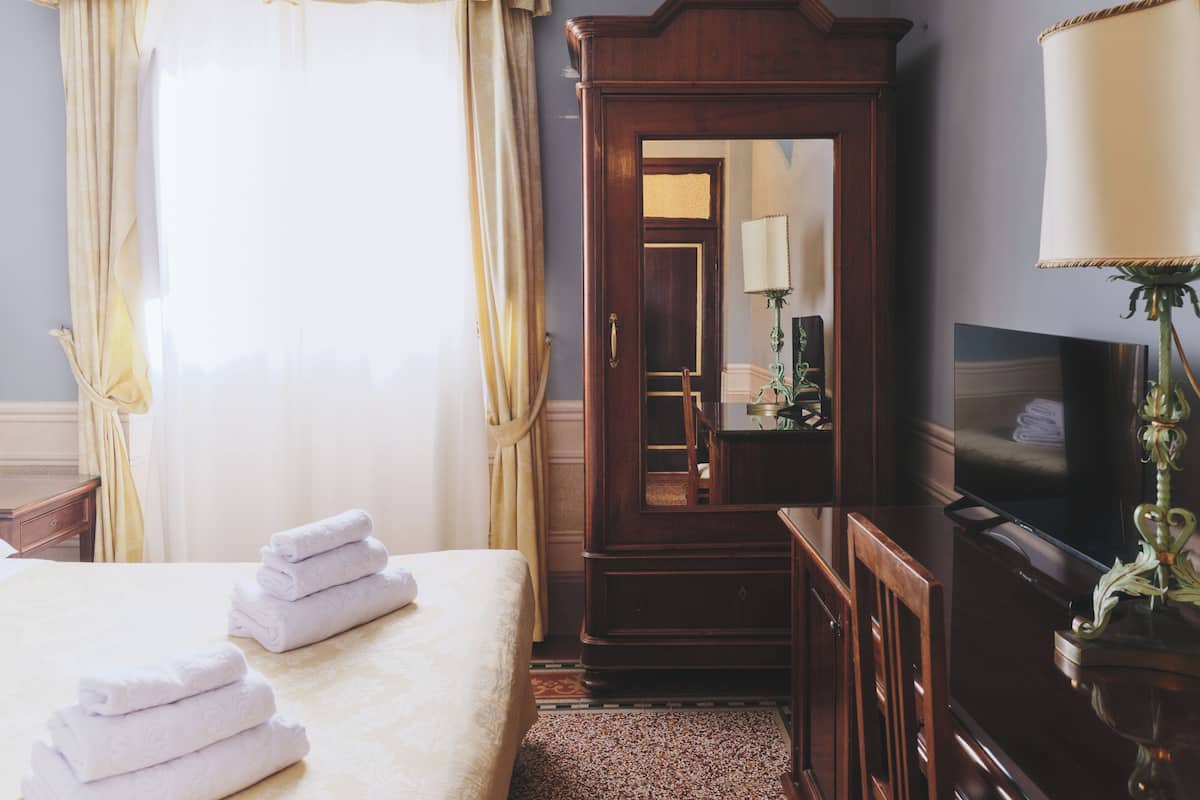 Ein Hotelzimmer mit einem Bett, einem Holzschrank, einem Schreibtisch mit Lampe und einem Fernseher.