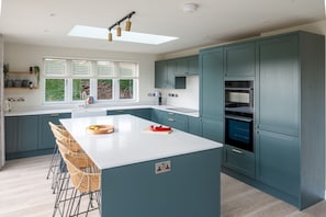 Une cuisine moderne dotée d’un îlot central, de meubles de couleur turquoise et d’une grande fenêtre qui laisse entrer la lumière naturelle.