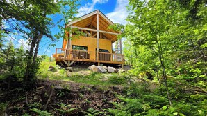 A wooden cabin with a balcony, surrounded by dense forest. - Nature & SPA | Chalet du Sommet (Sainte-Rose-du-Nord)