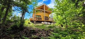 A wooden cabin with a balcony, surrounded by dense forest.