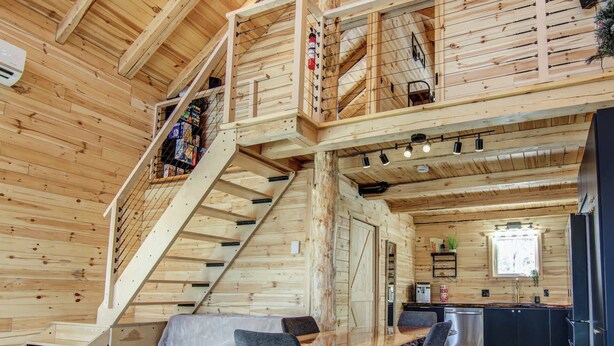A wooden cabin interior with a staircase, a dining area, and a kitchen. - Nature & SPA | Chalet du Sommet (Sainte-Rose-du-Nord)