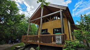 A wooden cabin with a balcony, surrounded by trees. - Nature & SPA | Chalet du Sommet (Sainte-Rose-du-Nord)
