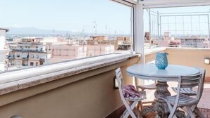 A balcony with a table and chairs, a view of the cityscape, and a wooden floor. - Cozy Penthouse with Terrace (Rome)