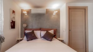A bedroom with a bed, two bedside tables, an air conditioner, a wall-mounted light fixture, and a door. - Cozy Penthouse with Terrace (Rome)