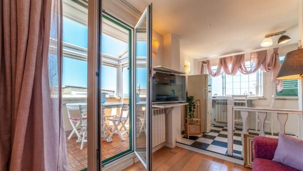 A compact living space with a kitchenette, a dining area, and a balcony with a checkered floor. - Cozy Penthouse with Terrace (Rome)