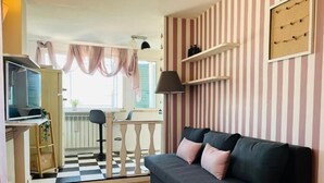 A living room with a sofa, a television, a small table, and a balcony with curtains. - Cozy Penthouse with Terrace (Rome)