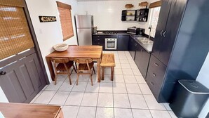 A compact kitchen with a dining table, chairs, a refrigerator, an oven, and a black cabinet.