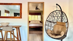 A room with a wooden dining table, a hanging chair, a bed with a view, and a mirror on the wall.