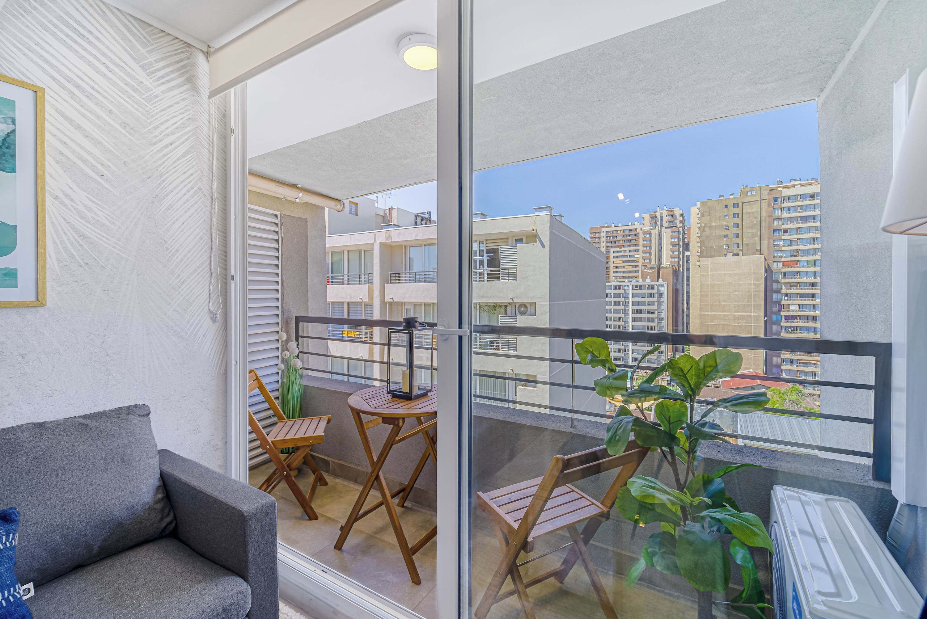 A balcony with a sofa, two wooden chairs, a small table, and a potted plant.