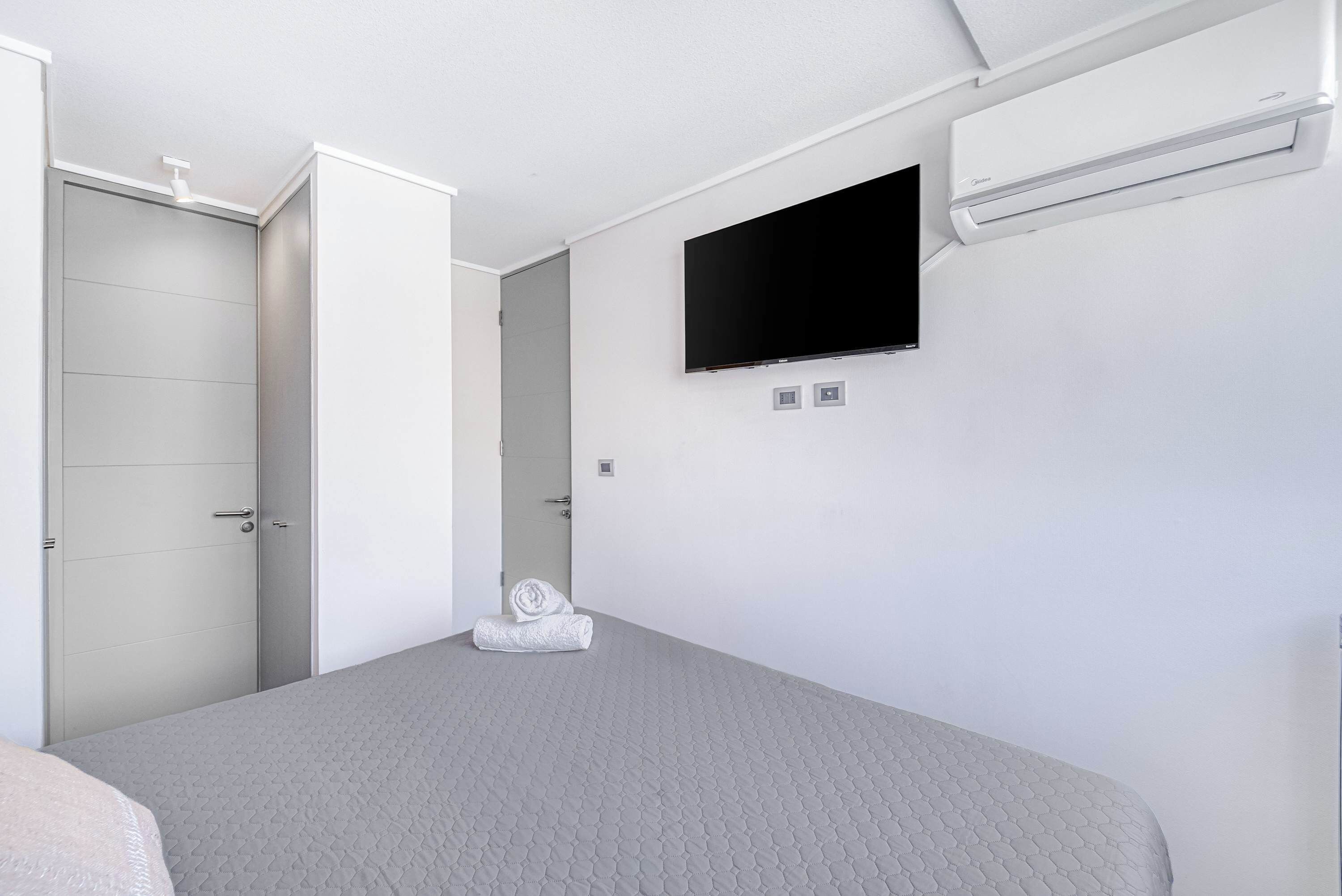 Ein Hotelzimmer mit einem Bett, einem an der Wand montierten Flachbildfernseher, einer Klimaanlage und einer Tür zu einem weiteren Raum.