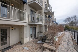 A multi-story residential building with balconies, a brick pathway, and a small outdoor seating area.
