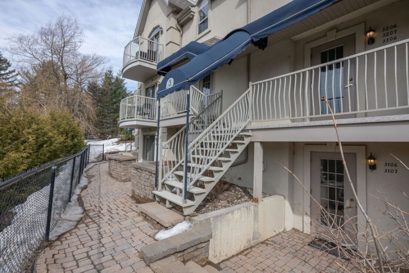 Un immeuble à plusieurs étages, doté d’un escalier menant à l’étage supérieur, d’un espace extérieur couvert et d’une allée piétonne délimitée par une clôture.