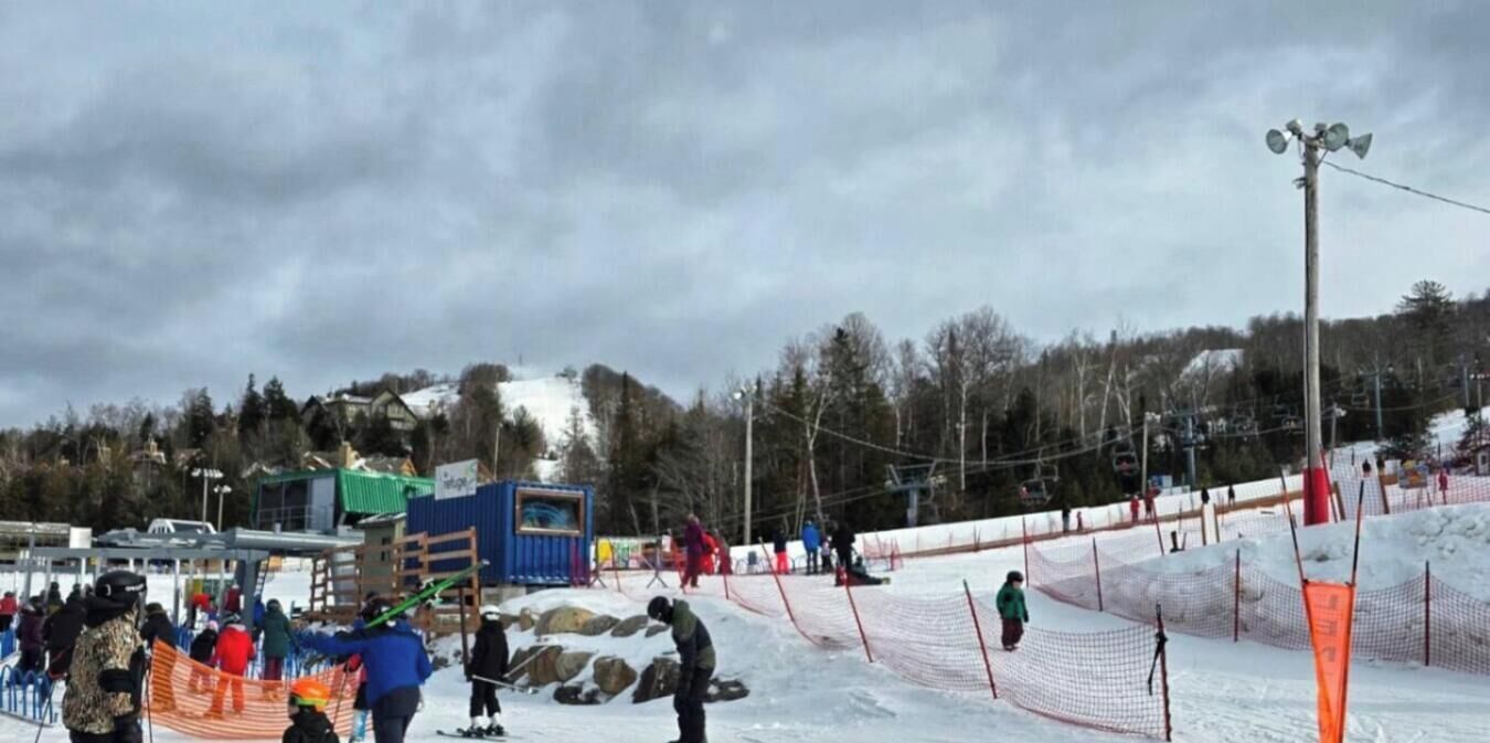 Eine Skipiste mit einem durch Netze gesicherten Bereich, einer Holzkonstruktion und bewölktem Himmel.