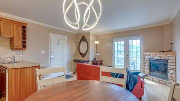 A dining area with a round table, wooden chairs, a pendant light, a fireplace, and a view through a window.