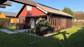 Une maison à deux étages avec une façade rouge, une véranda en bois et une balançoire.