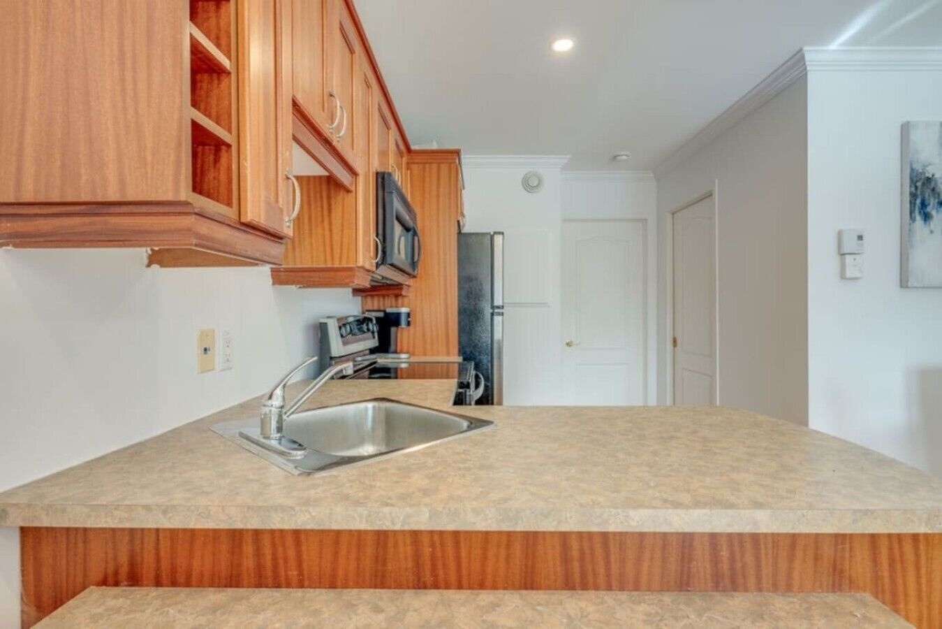 Cocina con armarios de madera, un lavamanos de acero inoxidable y un microondas.