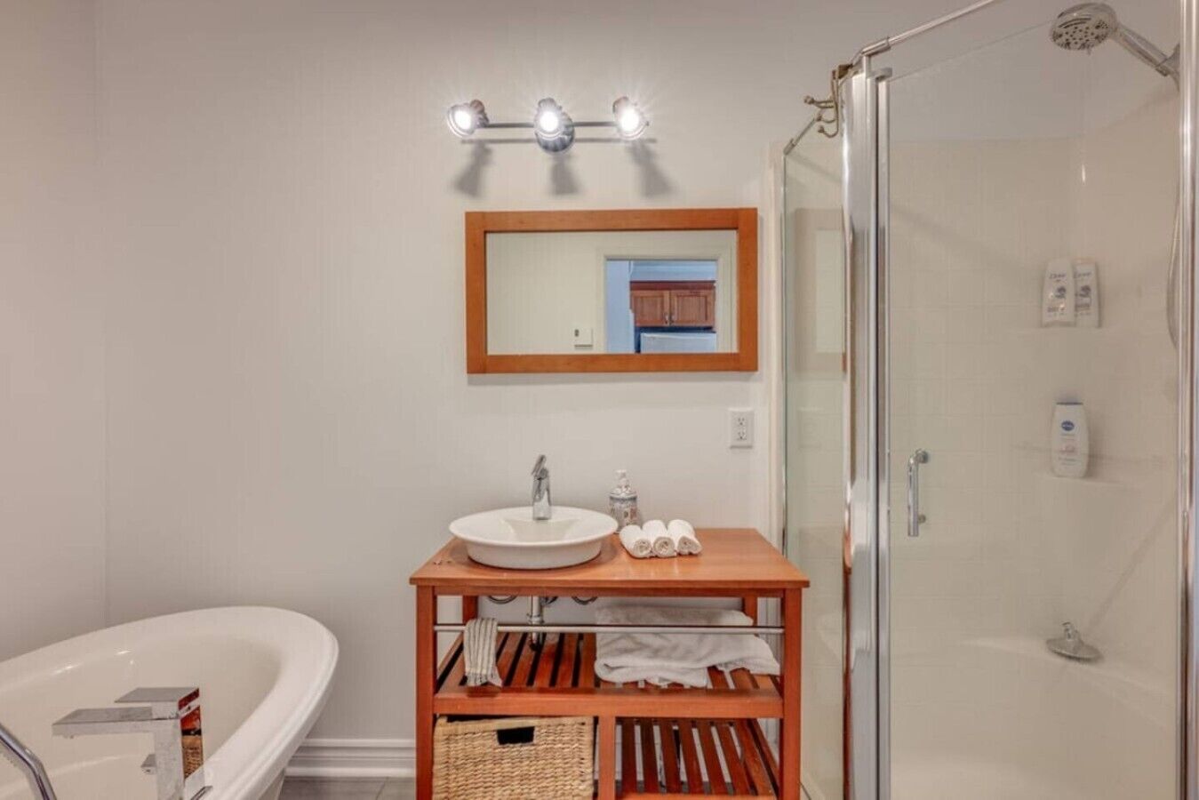 A bathroom with a white bathtub, a wooden vanity with a sink, a mirror, and a glass-enclosed shower.