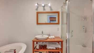 A bathroom with a white bathtub, a wooden vanity with a sink, a mirror, and a glass-enclosed shower.